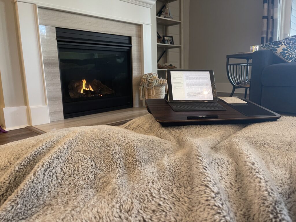 A photograph of an ipad on a lapdesk in front of a fireplace.